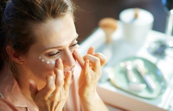 A woman applies eye cream over her vanity.