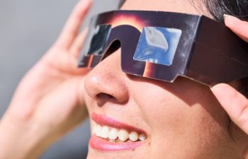 A woman views a solar eclipse while wearing glasses.